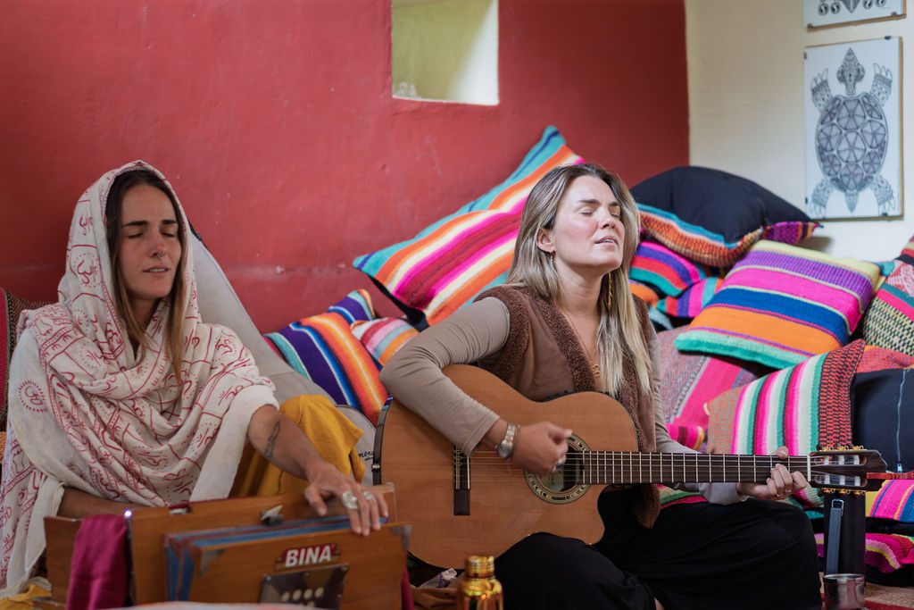 Two women play harmonium and guitar during an evening ceremony