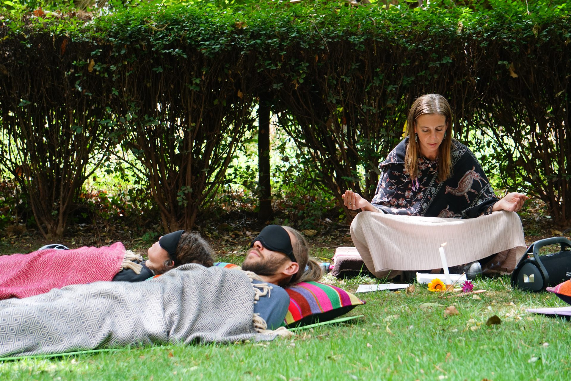 A facilitator sits before a circle of participants resting on the lawn