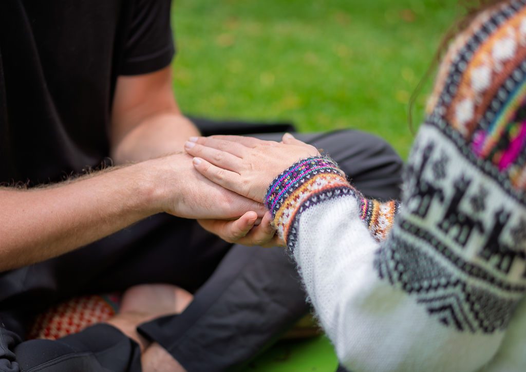 Two people hold hands during a sharing circle, one wearing an Andean knit sleeve