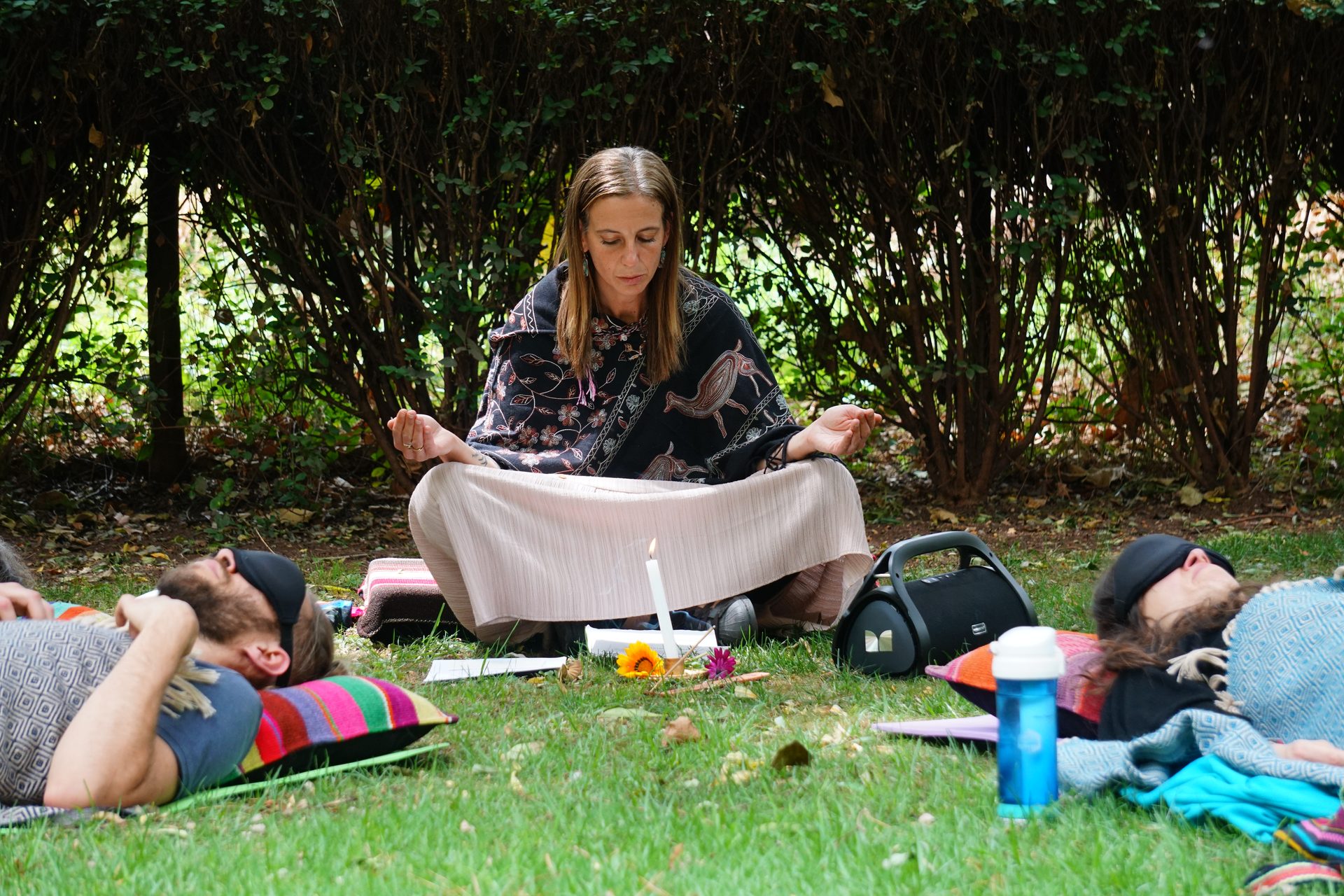 A facilitator teaches a circle of students sitting on the garden lawn