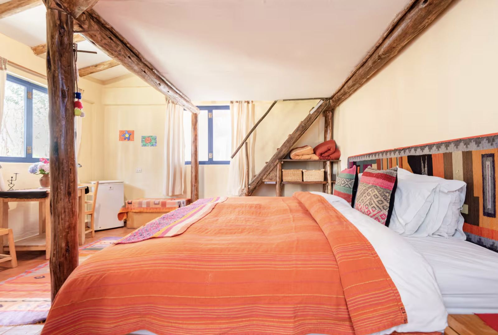 Double bed with an orange blanket under wooden beams