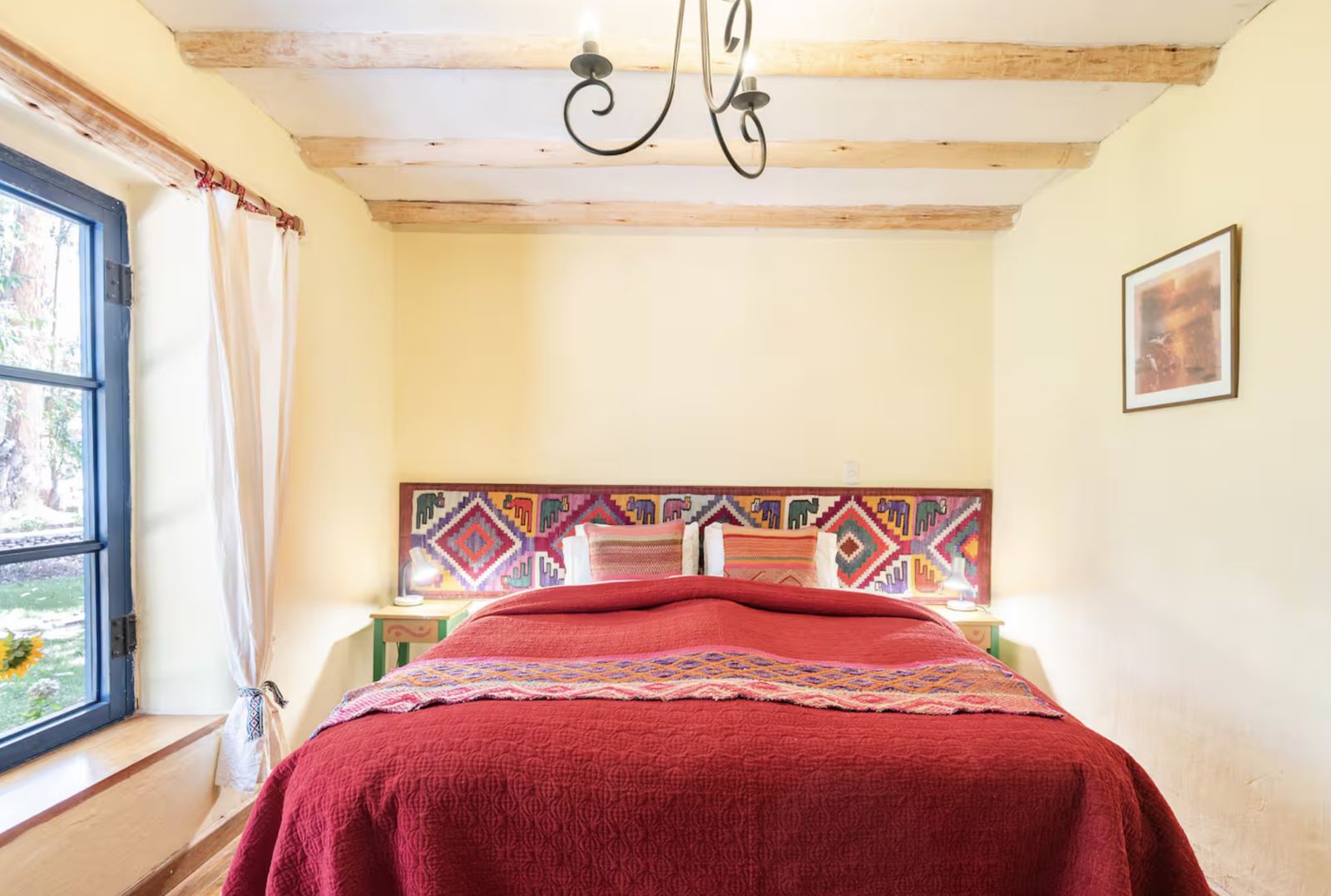 Bright bedroom with a red bedspread, an Andean textile headboard and a garden window